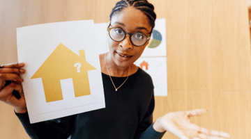 woman shrugging with picture of a house in-hand