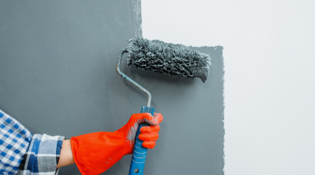 painter with orange glove rolling gray paint on a wall