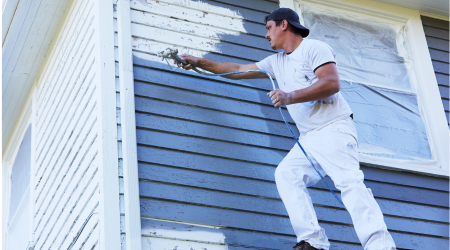 painter applying blue paint to exterior of home