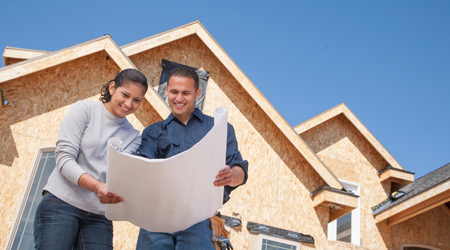 Couple reviewing blueprint in front of new construction