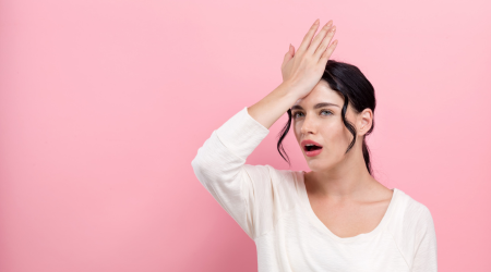 woman with hand on forehead pink wall